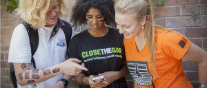 Students huddle around a mobile phone to showcase their interest in the Close the Gap Instagram challenge