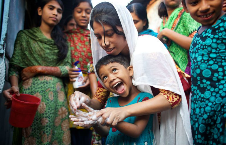 A teenage girl shows a small child how to wash her hands properly in Bangladesh