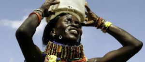 a smiling woman carries a bucket of water on her head