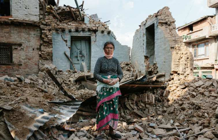 a woman stands in front of rubble and a demolished building