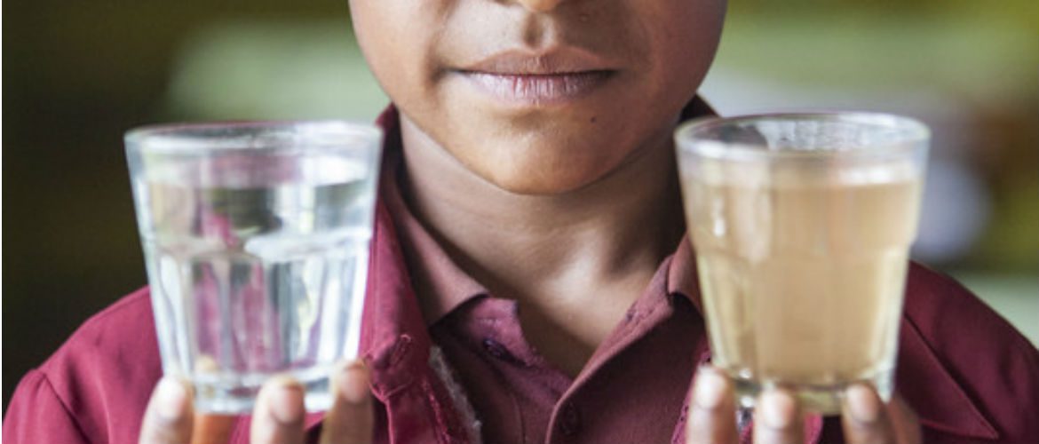 A student holds two glasses of water to show the difference in water quality in her school in PNG