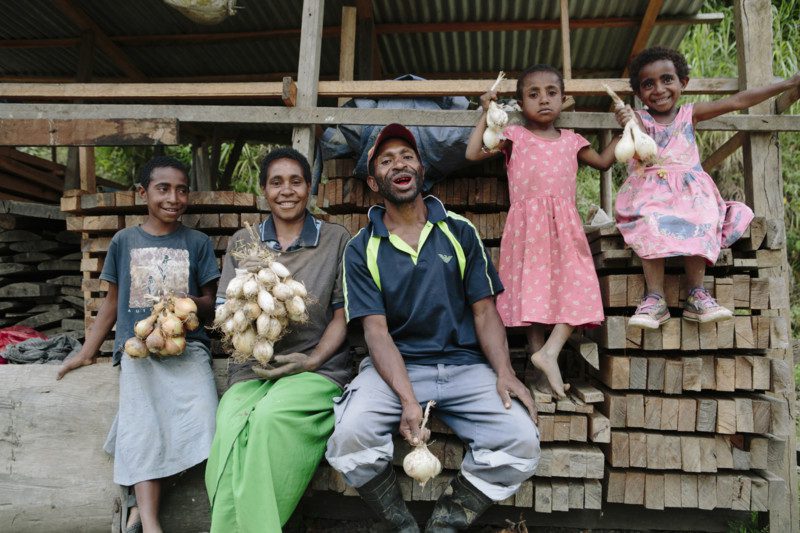 A family sit on building supplies holding onions