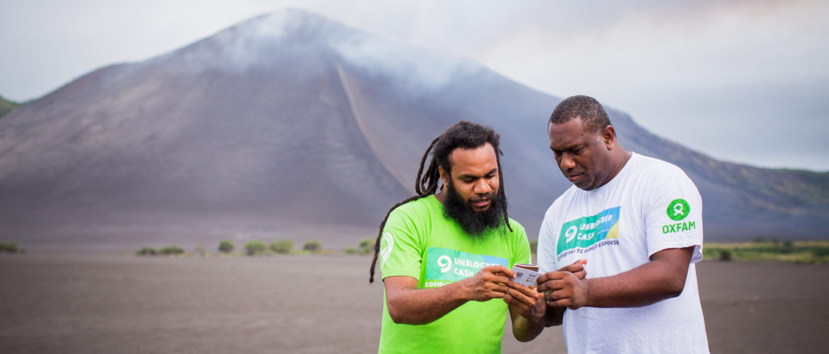 Tanna, Vanuatu: While Vanuatu’s largest volcano, Mount Yasur, smoulders in the distance, Oxfam staff Keith and Sirus test cards and phones that will be distributed to local community members for use within Oxfam’s UnBlocked cash transfer program. Photos: Arlene Bax/Oxfam in Vanuatu