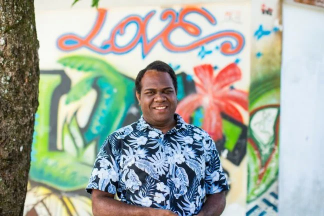 Yannick stands in front of a wall of street art with the word love. Yannick is the program manager of Vanuatu Pride (VPride). Oxfam acknowledges the support of the Australian Government through the Australian NGO Cooperation Program (ANCP).
