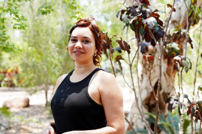 Yawuru (Broome), Australia: Obby participated in the KAWC Roundtable in Broome, 2023. She is a proud Bunuba woman from Fitzroy Crossing. Photo: Aimee Han/Oxfam Obby stands smiling at the camera in front of some trees in Yawuru (Broome), Australia. Obby participated in the KAWC Roundtable in Broome, 2023. She is a proud Bunuba woman from Fitzroy Crossing.