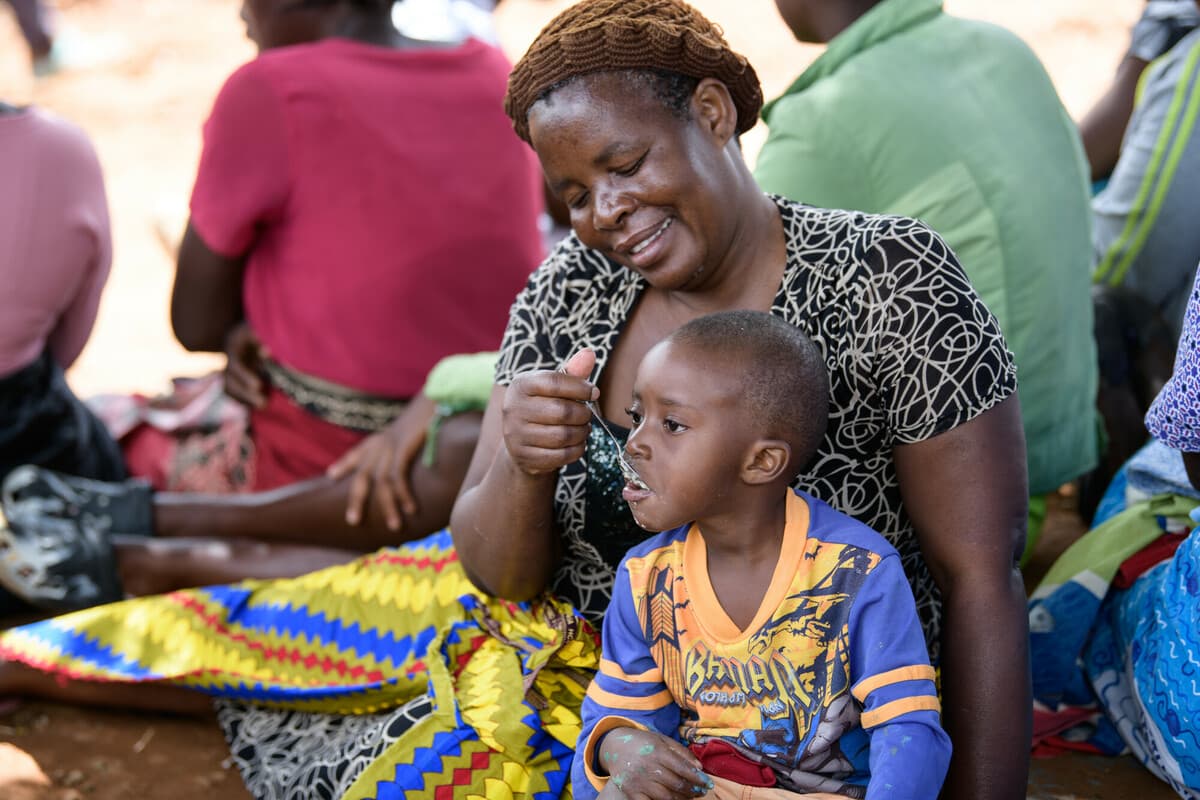 Malawi: Manesi, feeding 5-year-old Chimwemwe* porridge at a displacement camp in Blantyre southern Malawi on Saturday 25 March 2023. Thoko Chikondi / Oxfam Malawi: Manesi, feeding 5-year-old Chimwemwe* porridge at a displacement camp in Blantyre southern Malawi on Saturday 25 March 2023. Thoko Chikondi / Oxfam